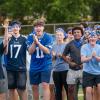 A large group of students wearing blue bandanas and other blue clothing clap and cheer while standing on a sideline.