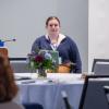 A student speaks into a microphone in a room where people are seated around round tables.