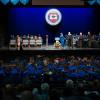 Graduates in graduation caps and gowns are visible sitting in the audience in the foreground as a graduate shakes the hand of Penn College President Michael J. Reed on the stage of the Journey Bank Community Arts Center. The Penn College seal is hanging agains a blue curtain at the back of the stage.