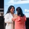 Standing on Penn College's Klump Academic Center stage, a woman adds a pin to a physician assistant student's white lab coat.
