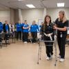 Nursing students watch as two physical therapist assistant students demonstrate how to guide a person in a walker.