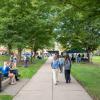 Students gather on the sidewalk and lawn area on the west side of Penn College's Bush Campus Center. Cornhole sets and canopies are visible in the background.