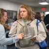 A student holding a Pennsylvania College of Technology Transition Conference drawstring bag speaks with Dawn M. Dickey in the conference’s vendor exhibit area, while other attendees visit displays in the background.