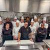 Culinary arts students and a faculty member pose a kitchen at Penn College with Visiting Chef Rob Wood. All are wearing chefs uniforms or waitstaff uniforms.