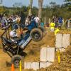 Penn College’s Baja SAE vehicle climbs a dirt obstacle during an off-road endurance competition while spectators watch from behind a safety barrier.